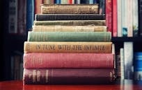 A stack of vintage hardcover books on a wooden table in a cozy library setting.